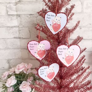 May include: Four pink and white heart-shaped ornaments with a white kitten holding a red heart that says "Hello Happy Valentine's Day". Each ornament has the text "You Are Purr-fect" on it.