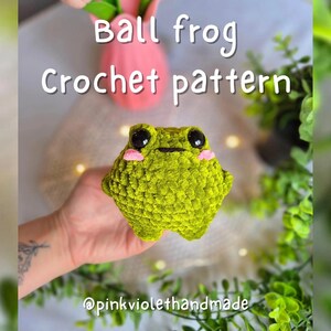 Può includere: Un piccolo rospo a forma di palla verde all'uncinetto con occhi neri e guance rosa. Il rospo è tenuto in una mano. Il testo "Ball frog Crochet pattern" è in alto nell'immagine. Il testo "@pinkviolethandmade" è in basso nell'immagine.