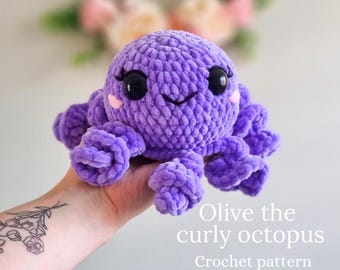 May include: A crocheted purple octopus with a smiling face and curly tentacles. The octopus is being held in a hand. The text "Olive the curly octopus Crochet pattern" is below the octopus.