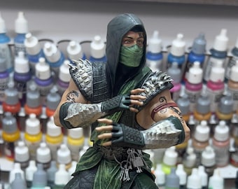 Könnte beinhalten: Eine grün-schwarze Actionfigur eines Ninja-Kriegers mit grüner Maske und schwarzer Kapuze. Die Figur steht auf einem sechseckigen Sockel mit einem detaillierten Design.
