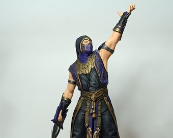 Könnte beinhalten: Eine lila und goldene Actionfigur eines maskierten Charakters, der eine Waffe hält. Die Figur steht auf einem schwarzen runden Sockel mit einem detaillierten Design.