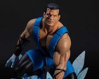 May include: A detailed figurine of a muscular character in a dynamic pose. The figure wears a blue and black outfit with white gloves. The character is kneeling on a base of ice, with a splash of water. The figure has a scar on the face.