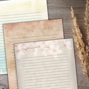 May include: Three sheets of lined paper with different backgrounds. The top sheet is a light yellow with a subtle texture. The middle sheet is a light brown with a subtle texture. The bottom sheet is a light gray with a subtle texture and a floral design of white flowers.