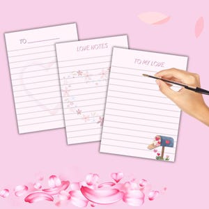 May include: Three lined notepads with romantic themes. One notepad has the text "TO" at the top, another says "LOVE NOTES", and the third says "TO MY LOVE". A hand is holding a pen over the third notepad. Pink heart and flower designs are visible.