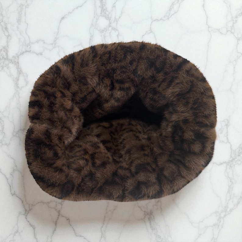 May include: A plush, brown pet bed with a leopard print pattern. The bed is circular and appears soft and comfortable, perfect for a small dog or cat. The faux fur material is a mix of dark and light brown tones.