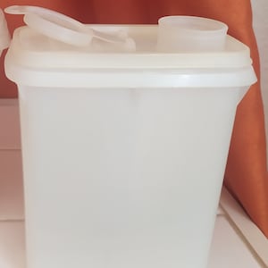Op de afbeelding: Een witte plastic container met een scharnierend deksel en een aparte giettuit. De container is ontworpen voor het bewaren van droge producten zoals ontbijtgranen of bloem.