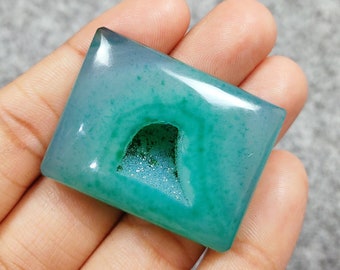 Op de afbeelding: Een lichtgroene agaat cabochon met een natuurlijk gat in het midden. De steen heeft een doorschijnende, bijna matte uitstraling.