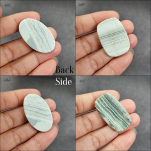 May include: Four oval and rectangular shaped green and white agate cabochons. The cabochons are smooth and polished. The cabochons are displayed on a hand.