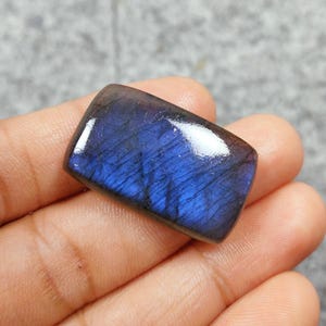 May include: A rectangular, dark blue labradorite gemstone with iridescent flashes of color. The gemstone is polished and has a smooth surface.