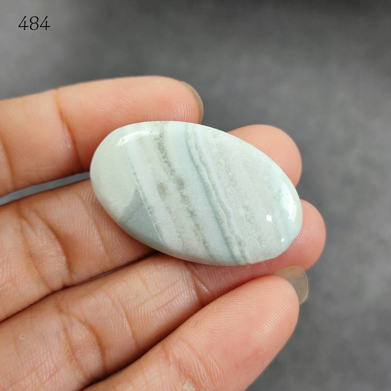 May include: A light green and white oval cabochon gemstone with a banded pattern. The stone is smooth and polished.