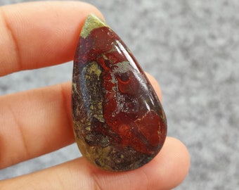 Könnte beinhalten: Ein tropfenförmiger Cabochon aus rotem, grünem und braunem Jaspis mit polierter Oberfläche. Der Stein hat ein wirbelndes Muster aus Farben und ist bereit, in Schmuck eingefasst zu werden.