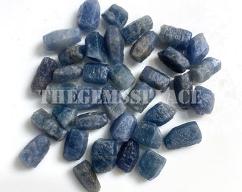 May include: A collection of rough, blue sapphire gemstones. The gemstones are various sizes and shapes, with a natural, unpolished finish.