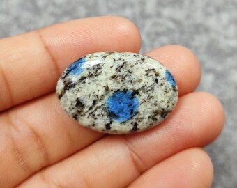 May include: Oval-shaped blue and white gemstone with a speckled pattern. The gemstone has a smooth, polished surface.