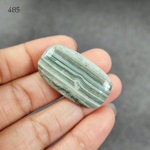 May include: A green and white banded agate cabochon with a smooth, polished surface. The stone has a natural, organic pattern.