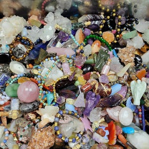 Può includere: Una collezione di varie pietre preziose e cristalli in una varietà di colori. L'immagine include punte di ametista, grappoli di quarzo, perline e piccole bottiglie. Ci sono anche figurine di angeli scolpite e sfere lucide. La disposizione è densa e colorata.