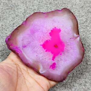 Puede incluir: Una rebanada de ágata pulida de forma irregular. La piedra presenta un centro rosa vibrante que se desvanece a rosa claro y blanco, con un borde exterior marrón oscuro. El ágata es un artículo decorativo.