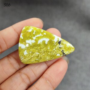 Pode incluir: Um cabochão verde e branco com forma triangular. A pedra tem um padrão manchado de verde e branco.