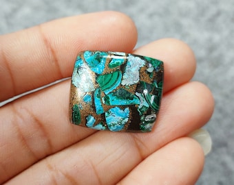 May include: A square-shaped, green, blue, and gold gemstone cabochon with a unique, marbled pattern. The gemstone is set in a clear, resin-like material.