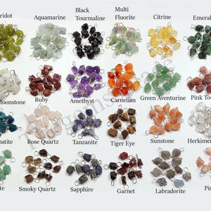 May include: A selection of raw gemstone beads in a variety of colours, such as green peridot, blue aquamarine, black tourmaline, and purple amethyst. Each gemstone is labelled with its name and has a silver loop attached.