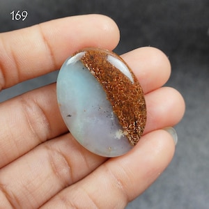 May include: Oval shaped cabochon gemstone with a light blue and white base and a brown, rust-colored band across the top.