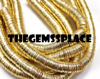 May include: A strand of gold-coloured metal beads, each bead is a flat, round disc with a slightly textured surface. The beads are stacked on top of each other, creating a long, continuous chain. The image is taken from a close-up perspective, showing the details of the beads.