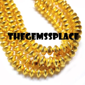 May include: A close-up of a gold-colored beaded necklace. The beads are round and have a textured surface. The necklace is arranged in a spiral pattern.