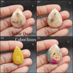 May include: Four teardrop-shaped solar quartz cabochons in various colors and patterns. The cabochons are displayed on a hand, with the text "Solar Quartz Cabochons" printed below them.