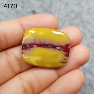 May include: A yellow and red banded gemstone cabochon. The stone has a smooth, polished surface and is held in a hand.