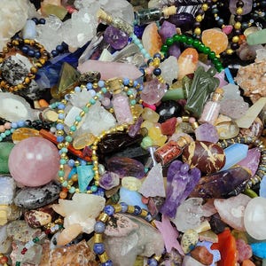 May include: A collection of various gemstones, crystals, and beads in a variety of colors. The image includes quartz crystals, amethyst, rose quartz spheres, and beaded necklaces. There are also small glass bottles with cork stoppers and carved angel figurines.