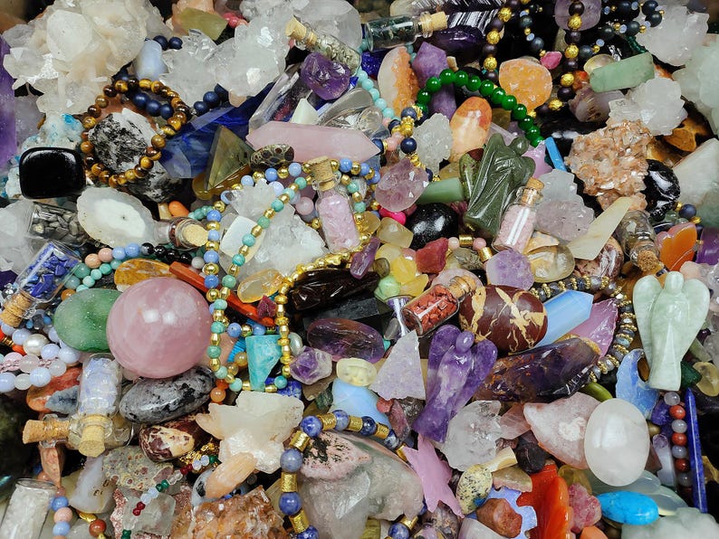 May include: A collection of various gemstones, crystals, and beads in a variety of colors. The image includes quartz crystals, amethyst, rose quartz spheres, and beaded necklaces. There are also small glass bottles with cork stoppers and carved angel figurines.
