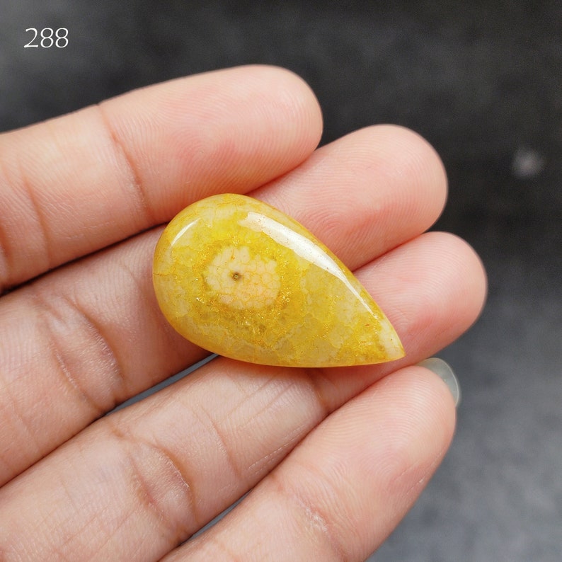 May include: A teardrop-shaped yellow gemstone with a white and pink flower-like pattern inside.