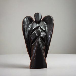 May include: Black obsidian angel figurine with detailed carvings. The angel is standing with its wings spread out.