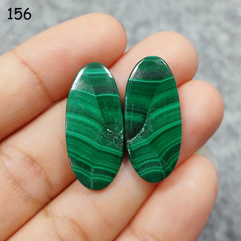 Puede incluir: Dos cabujones ovalados de malaquita verde con un patr&oacute;n de remolino.