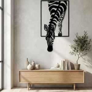 Può includere: Arte da parete in metallo bianco e nero raffigurante una zebra. La zebra è mostrata dal collo in giù, con la testa abbassata. L'opera d'arte è montata su una parete bianca sopra un mobile in legno.