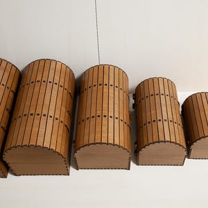 Puede incluir: Cinco arcones de almacenamiento de madera de diferentes tamaños están dispuestos en fila. Los arcones son cilíndricos con la parte superior e inferior curvadas, y están construidos con listones de madera verticales con detalles en marrón oscuro. Los arcones son de color marrón claro.