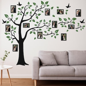 May include: A black tree wall decal with green leaves and black picture frames. The frames contain photos of couples. Decorative birds are also included in the design. A gray sofa and small table are in the foreground.