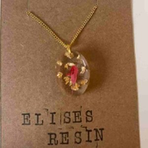 May include: Gold chain necklace with a clear oval pendant containing a red flower and gold flakes. The pendant is labelled "Elises Resin".