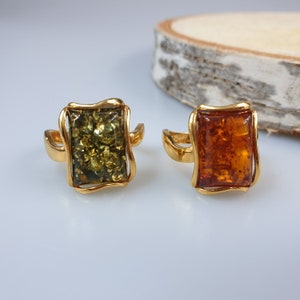 May include: Two gold rings with square amber stones. One ring has a green amber stone and the other has a brown amber stone.
