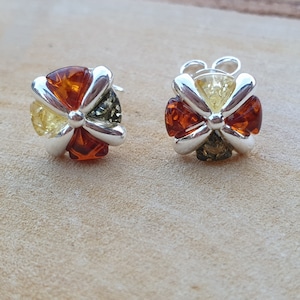 May include: A pair of silver earrings with a flower design. Each earring features five amber stones in shades of yellow, orange, and green.