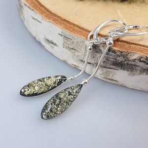 May include: A pair of silver dangle earrings with green and gold amber teardrop-shaped stones.