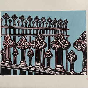 Puede incluir: Una impresión de una valla decorativa de hierro forjado con pináculos ornamentados sobre un fondo azul claro. La valla es negra con detalles rojos, y la obra está enmarcada en blanco.