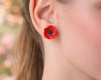 Può includere: Un orecchino a lobo a forma di fiore di papavero rosso con un centro nero testurizzato. Il fiore presenta petali arrotondati e sovrapposti in una tonalità rossa vibrante, creando un aspetto floreale realistico sul lobo.