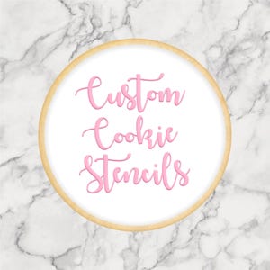 May include: A round cookie with a light brown edge and a white center. The words "Custom Cookie Stencils" are written in pink cursive script across the center of the cookie. The background is a marble pattern.