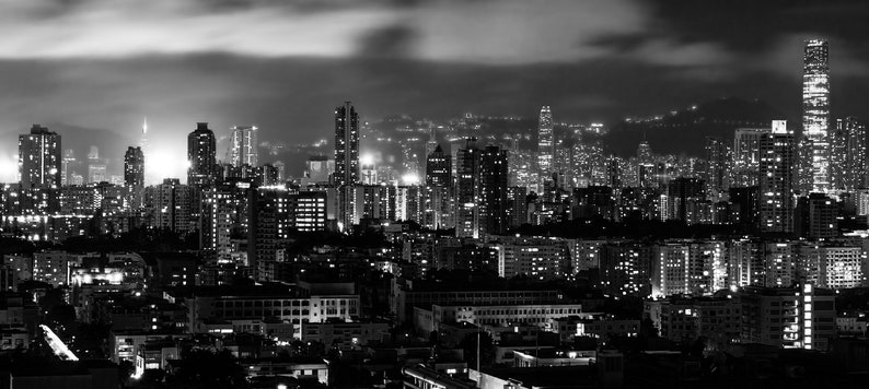 May include: A black and white photograph of a city skyline at night. The city is lit up with lights, and the buildings are tall and slender. The sky is cloudy and dark.