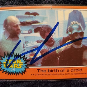 May include: A vintage Star Wars trading card featuring a scene from the film. The card shows three men, one wearing a droid helmet. Text on the card reads "The birth of a droid" and "Star Wars 313".