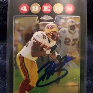 May include: A Topps Chrome trading card featuring Patrick Willis in a white and gold 49ers uniform. The card has a black border, the text 49ERS in red and gold circles at the top, and a blue ink autograph across the center of the player image.