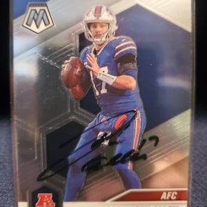 Peut inclure: Une carte de collection de football américain Panini Mosaic représentant Josh Allen des Buffalo Bills en uniforme bleu. La carte présente un autographe à l'encre noire au centre, le logo AFC, ainsi que le texte Josh Allen et Buffalo Bills en bas.