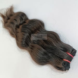 Puede incluir: Un paquete de extensiones de cabello ondulado de color marrón oscuro. El cabello está atado con una banda elástica roja. El cabello tiene un aspecto y una textura naturales, con diferentes tonos de marrón.