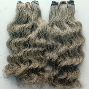 May include: Two bundles of wavy gray human hair extensions. The hair is a light gray color with some darker gray strands.