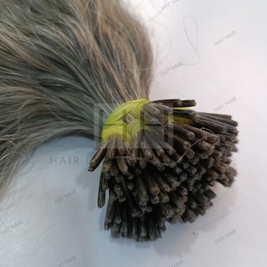 May include: A bundle of gray human hair extensions with pre-bonded keratin tips. The hair is tied together with a yellow rubber band.